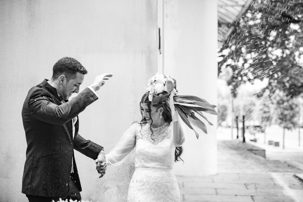 A black and white candid photo of bride and groom as they are trying to shield themselves from the rice that wedding guests are throwing on them as they exit the townhall.