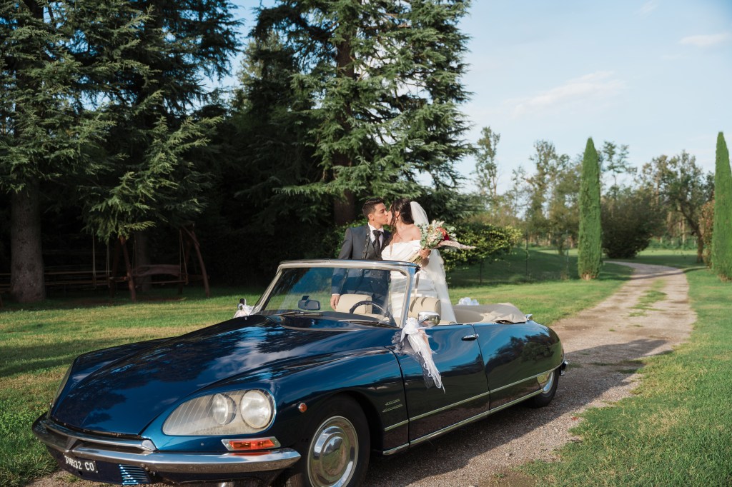 The couple is kissing while standing inside a roofless vintage car