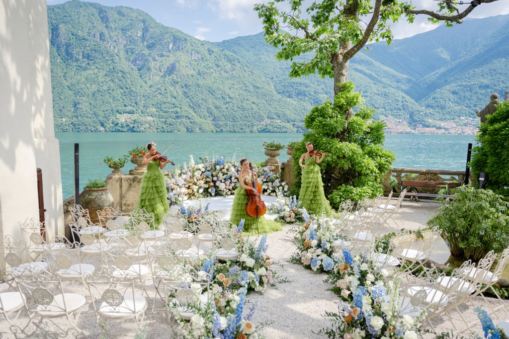 A gorgeous wedding ceremony set up next to the church at villa del Balbianello. Three violinists in green dresses are standing aroung the "altar"