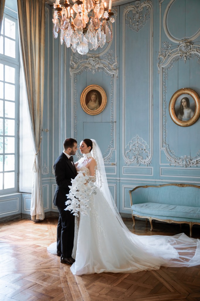 The couple is standing inside the blue room of Chateu de Champlatreux. They're hugging and looking into each other's eyes