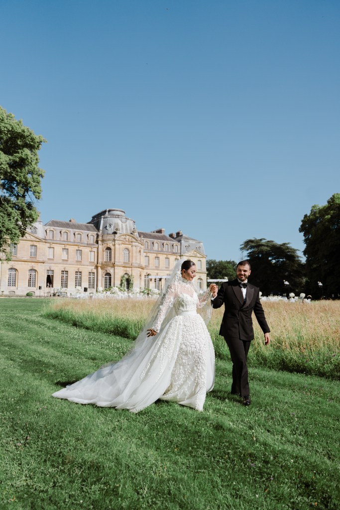 Bride and groom walking hand in hand in the field next to Chateu de Champlatreux