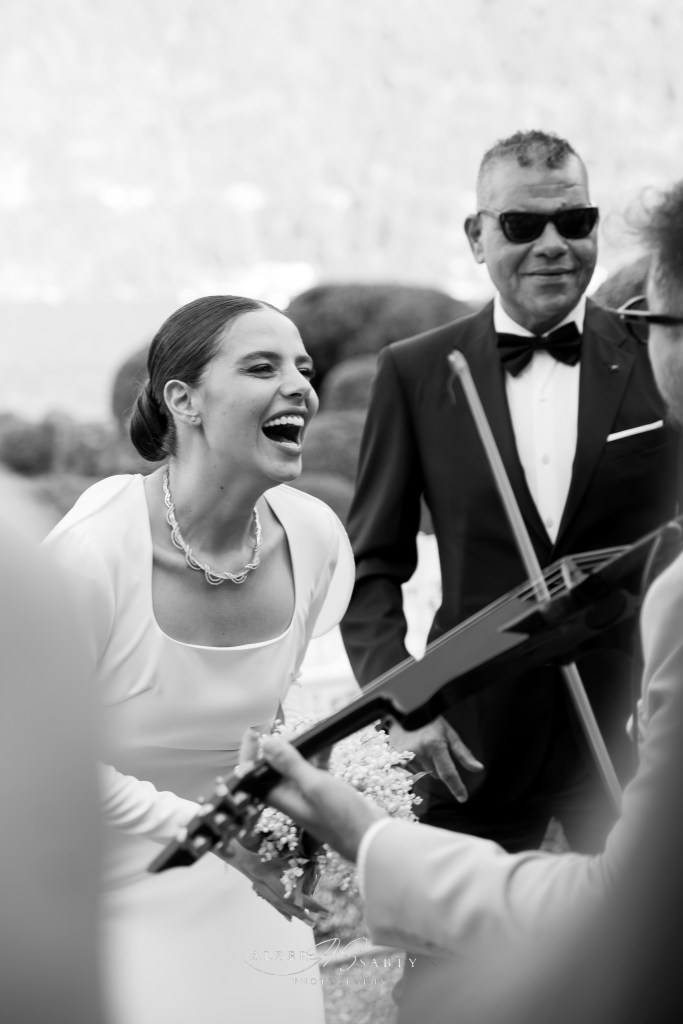 A black and white shot of the bride laughing while listening to a violinist playing her favourite song
