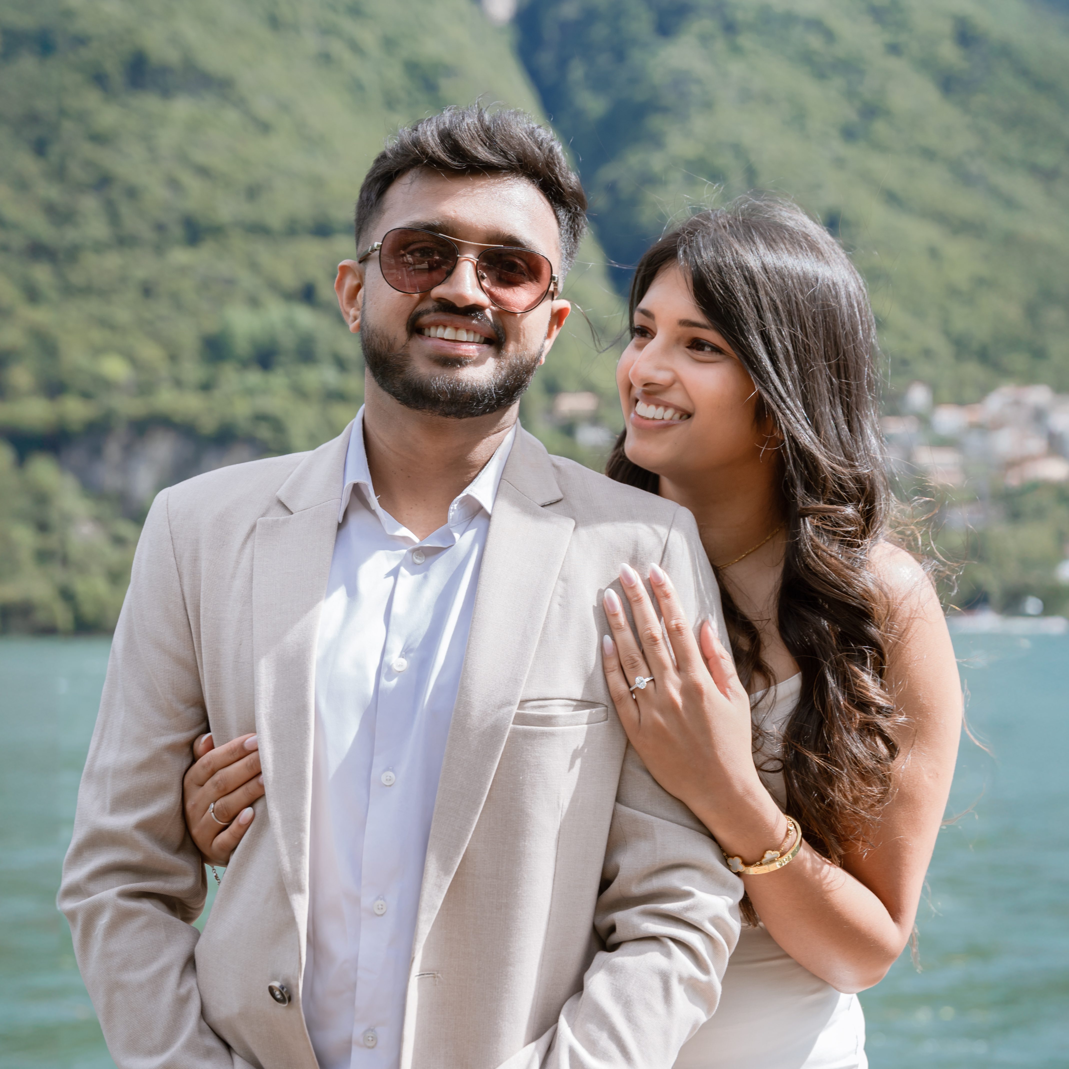 Couple posing with Lake Como and its mountains in the backround. The woman stands slightly behind her partner with her hand on his shoulder