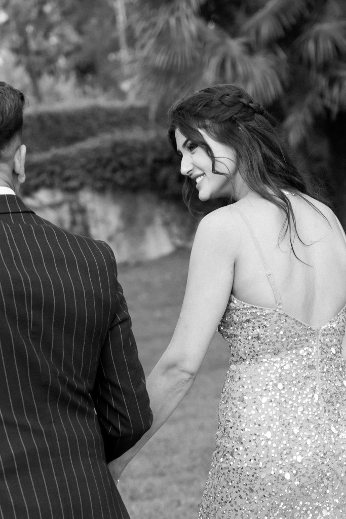 Candid photo of the couple walking away from the camera. The focus is on the girlfried looking playfully at her boyfriend