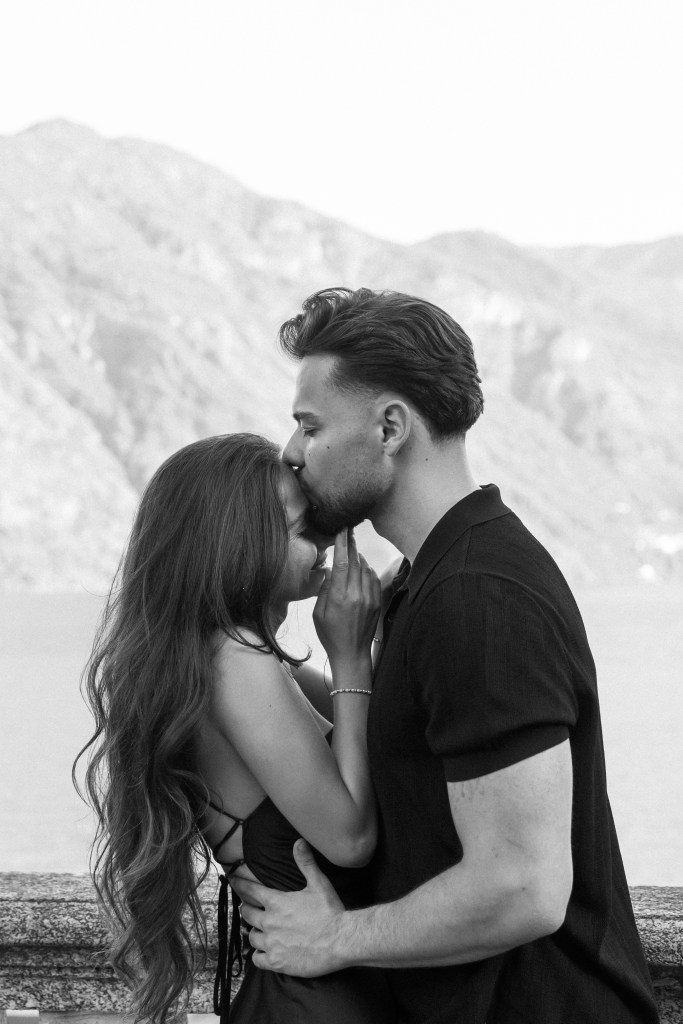 Black and white photo of the couple hugging each other closely, he is kissing her forehead