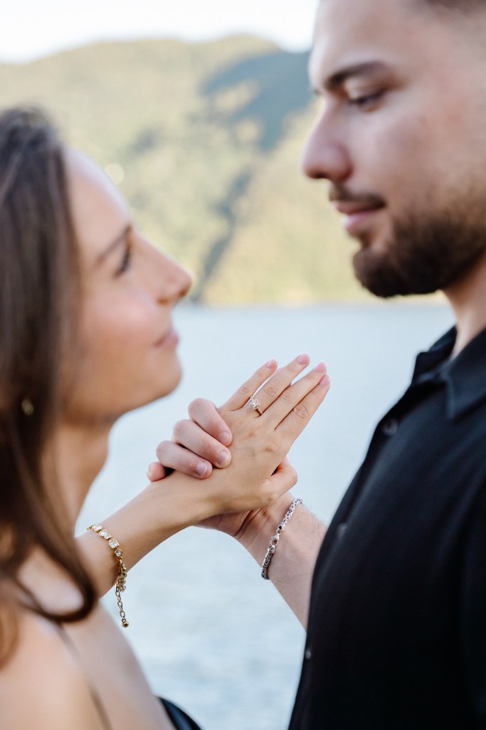 Close up portrait of a couple as they are looking into each other's eyes. In focus is their hands intertwined, showing her engagement ring